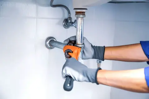 Hydraulik w rękawiczkach dokręca kluczem instalację pod zlewem.