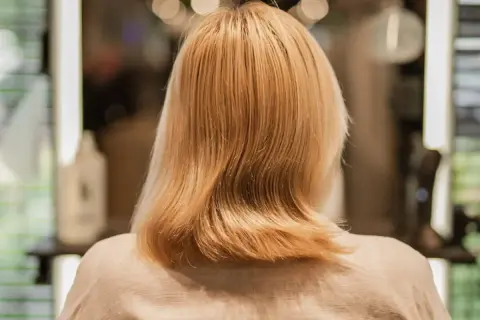 Kobieta z blond włosami, które zaczynają przechodzić w siwe. W tle widać salon fryzjerski.