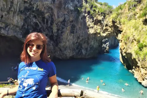 Giovane donna sorride in una baia con acqua turchese, uno dei tanti posti da visitare in Calabria.