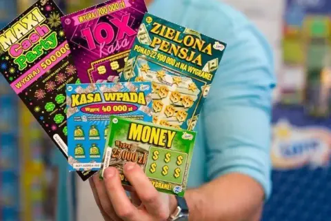 Dłoń trzyma kilka kolorowych zdrapek z napisami "Maxi Cash Party", "10X Kasa", "Zielona Pensja", "Kasa wpada" i "Money".