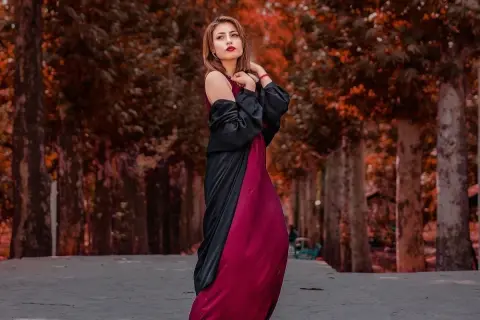 Elegancka kobieta w bordowej sukience i czarnym narzutce, idealne połączenie, które podpowiada, jakie dodatki do bordowej sukienki wybrać na jesienny spacer.