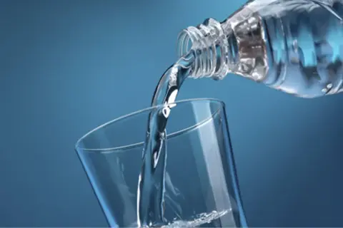 Un filet d'eau pure, riche en magnésium, se verse d'une bouteille dans un verre transparent sur fond bleu.