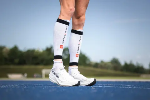 Manchons de compression mollet : pour une meilleure récupération et performance. Ces manchons blancs avec logo Compressport sont portés par un coureur.