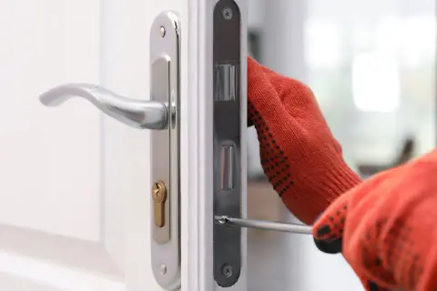 Main tenant utilise un tournevis pour changer la serrure d'une porte blanche.