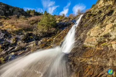 Cascada en un paisaje rocoso y seco, con vegetación escasa. El agua cae con fuerza, creando una estela blanca. Un rincón natural cerca de San Mamés, Madrid.