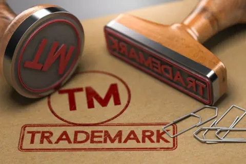 Dwa stemple z napisem "TRADEMARK" i symbolem "TM" na brązowym tle, obok spinaczy.