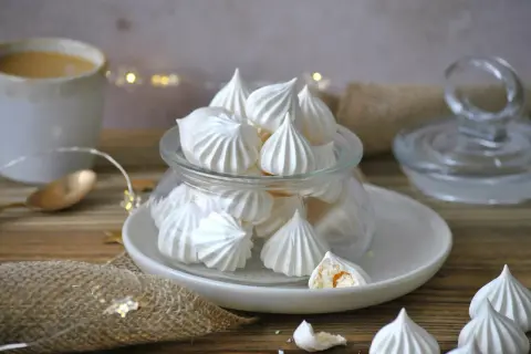 Leckeres Meringen Rezept: zarte Baiser-Häufchen in einem Glas, daneben eine Tasse Kaffee und Lichterkette.