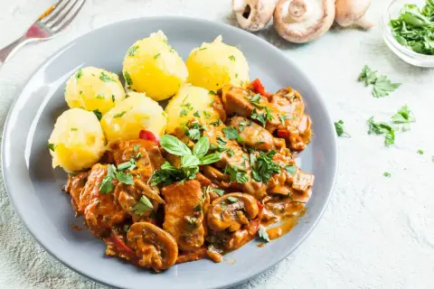 Pyszny gulasz z kurczaka z pieczarkami i papryką, podany z ziemniakami posypanymi natką pietruszki.