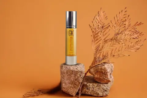 Sérum capilar GK Hair en envase dorado, con ramas secas y rocas. Descubre las maravillosas aceite de argan propiedades para tu cabello.