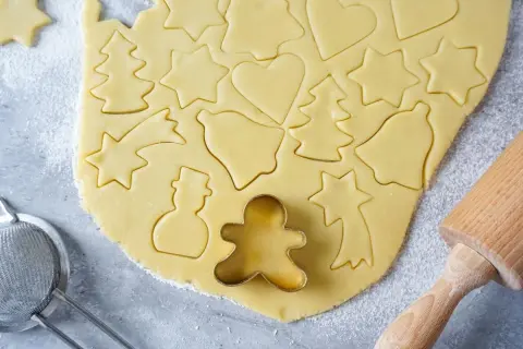 Ausgestochener Teig für Weihnachtsplätzchen mit Sternen, Herzen, Tannenbäumen und Schneemännern. Ein Ausstecher-Rezept für Spaß in der Küche.