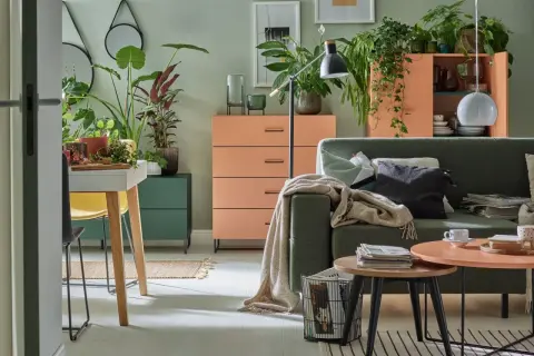 Salon z kanapą w kolorze zielonym i meblami w odcieniach pomarańczowego. Mnóstwo roślin tworzy przytulną atmosferę.