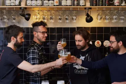 Amici brindano durante una visita birrificio. Bottiglie di birra e bicchieri in primo piano.