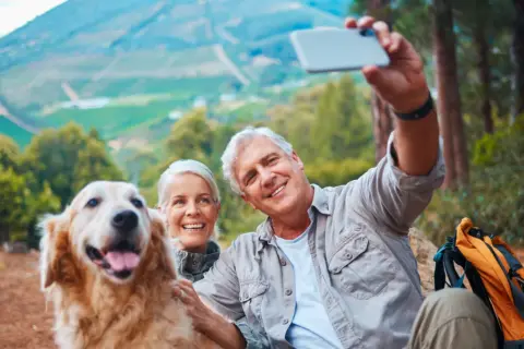 Couple prend un selfie avec leur chien lors d'une randonnée. Ils semblent heureux, profitant de la nature. Une belle journée pour faire garder son chien chez soi, loin des soucis.