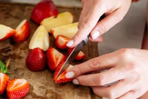 Hände schneiden Erdbeeren und Äpfel auf einem Holzbrett. Diese Früchte sind reich an Flavonoiden, die gut für die Gesundheit sind.