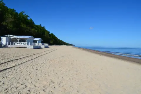 Plaża w Pobierowie z białymi budynkami i niebieskimi markizami, idealne miejsce na wakacyjne atrakcje nad morzem.
