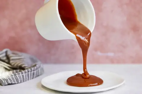 Flüssige Karamellsauce fließt aus einer weißen Kanne auf einen Teller. Ein einfaches karamellsauce rezept für süße Momente.