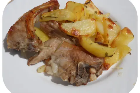Un succulento agnello gratinato al forno, servito con patate dorate e profumate al rosmarino su un piatto bianco.