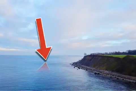 Roter Pfeil zeigt auf die Ostsee, wo sich Meerforellen-Hotspots befinden. Küste mit Steilküppe im Hintergrund.