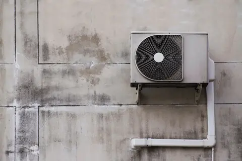 Unité extérieure d'une pompe à chaleur fixée à un mur en béton. Vérifiez l'éligibilité pompe à chaleur gouvernement pour des aides.