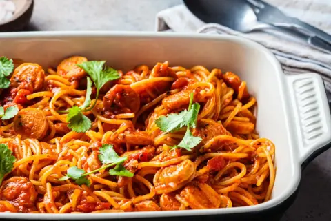 Pyszne spaghetti z kiełbasą w sosie pomidorowym, udekorowane kolendrą. Idealny pomysł, co zrobić z makaronem spaghetti na szybki obiad.