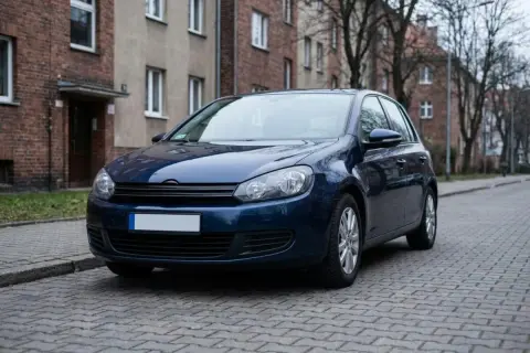 Ciemnoniebieski samochód stoi na ulicy z kostki brukowej. Brak tablic rejestracyjnych, co sugeruje rejestracja samochodu bez tablic.