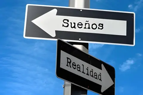 Señales de tráfico apuntan en direcciones opuestas: una hacia "Sueños" y otra hacia "Realidad". Frases de sueños y realidad.