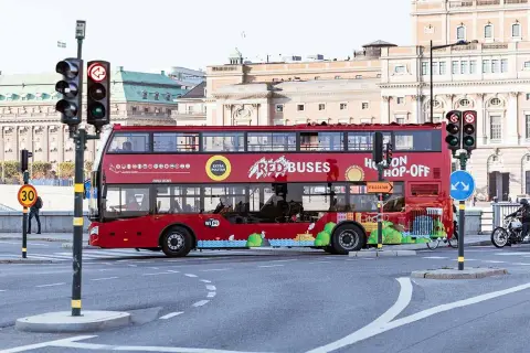 Röd dubbeldäckare för city sightseeing Stockholm passerar en korsning med trafikljus.