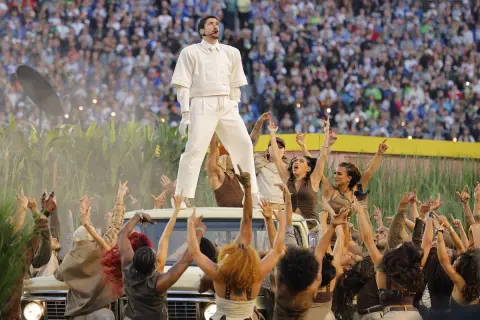 Bad Bunny na Super Bowl, otoczony przez tancerzy i tłum, na tle kukurydzy i stadionu.