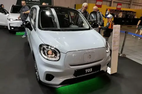 Biały Leapmotor T03 z czarnym dachem, prezentowany na wystawie. Obok samochodu stoją ludzie, w tym chłopiec w czapce.