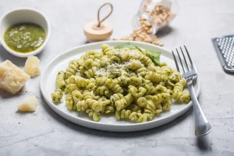 Pyszny makaron z pesto, posypany parmezanem, z dodatkiem świeżej bazylii i orzeszków piniowych.