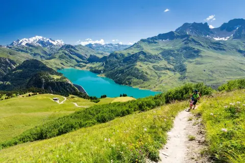 Une personne fait une rando alpes, profitant d'un lac turquoise et de montagnes majestueuses.