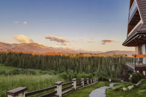 Widok z hotelu Kopieniec Murzasichle na Tatry o zachodzie słońca. Drewniany domek, kamienna ścieżka i las.