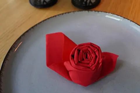 Un pliage serviette papier en forme de rose rouge sur une assiette grise. Une touche d'élégance pour une table.