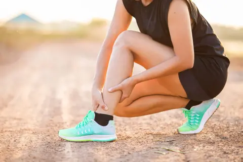 Une coureuse s'accroupit, se tenant le mollet, peut-être à cause d'une myalgie.