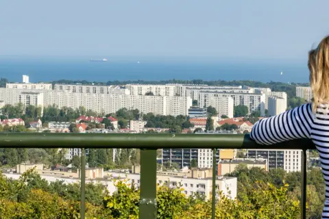 Widok z punktu widokowego w Oliwie na morze i osiedle. Kobieta w bluzce w paski podziwia panoramę.