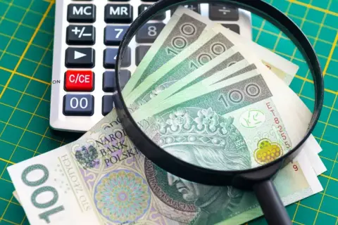 Kalkulator, lupa i polskie banknoty 100 zł na zielonym tle.