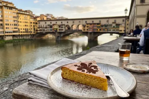 Ein Stück Schiacciata alla Fiorentina mit Kakaopulver-Dekor, serviert am Arno mit dem Ponte Vecchio im Hintergrund.