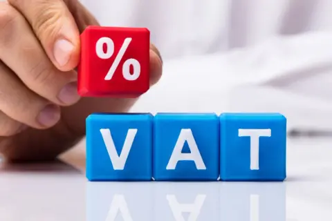 Dłoń układa kostkę z symbolem procentu na kostkach z napisem VAT. Czy to zapowiedź zmian w VAT na żywność?