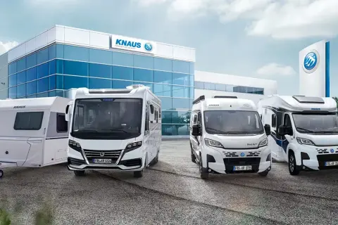 Una caravana y tres autocaravanas KNAUS blancas frente a un edificio moderno.