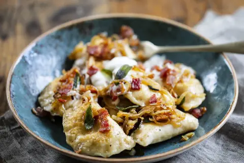 Pyszne pierogi z serem, okraszone skwarkami i cebulką, podane w niebieskiej misce.