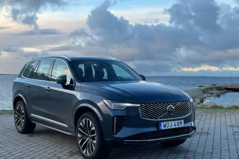 Elegancki, ciemnogranatowy Volvo XC90 2025 zaparkowany nad morzem, z chmurami na niebie.