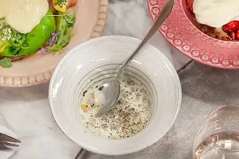En skål med krämig majs, kryddad med peppar, bredvid en tallrik med grönsaker och en rosa tallrik med jordgubbar och grädde.
