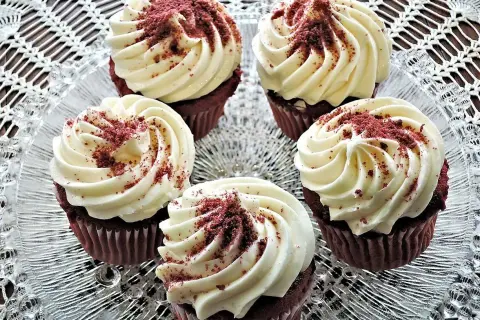 Fem röda sammetsmuffins med fluffig cream cheese frosting, strösslade med smulor.