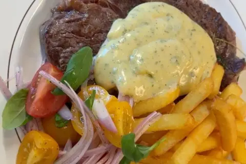 En saftig biff med krämig bearnaisesås, gyllene pommes frites och en fräsch tomatsallad. En klassisk steak frites-upplevelse.
