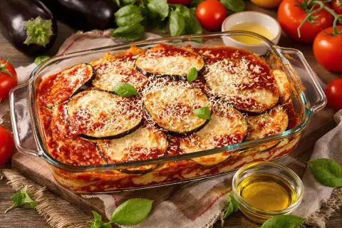Un plat d'aubergine parmigiana tout juste sorti du four, garni de fromage râpé et de basilic frais.