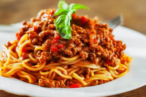 Porcja spaghetti bolognese z mięsem mielonym, sosem pomidorowym i bazylią na białym talerzu.