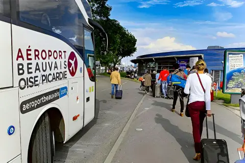 Autobus z napisem "AÉROPORT BEAUVAIS OISE/PICARDIE" czeka na pasażerów z walizkami przed terminalem.