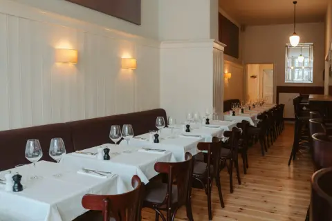 Elegantes Restaurant in Berlin, bereit für Gäste. Tische sind mit weißen Tischdecken, Gläsern und Besteck gedeckt. Gemütliche Atmosphäre dank Wandlampen.