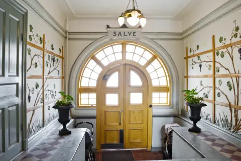 Entréhall med jugendstil hus-känsla. Dubbeldörrar med välvt fönster ovanför. Väggdekorationer med vinrankor.