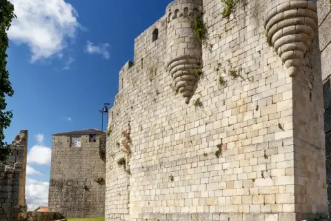 Muros de piedra de un castillo medieval en Castro Caldelas. Un torreón con matacanes y una torre con reloj son parte de lo que ver.